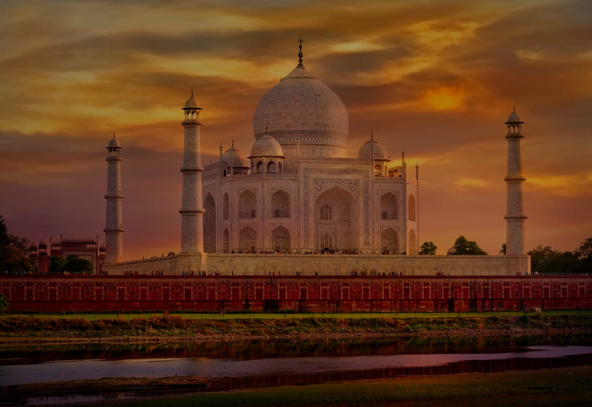 The Taj Mahal beneath a burning sunset sky, seen across the Yamuna riverbank at Agra