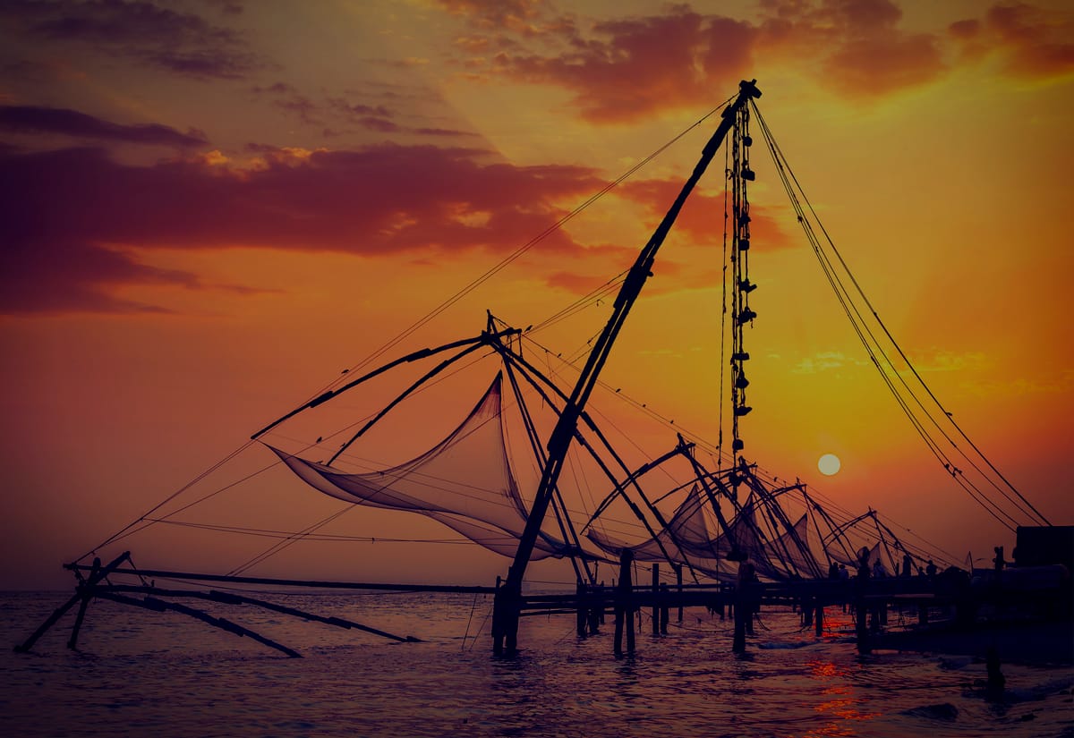 Cantilevered Chinese fishing nets silhouetted against a copper sunset on the Kerala backwaters at Kochi